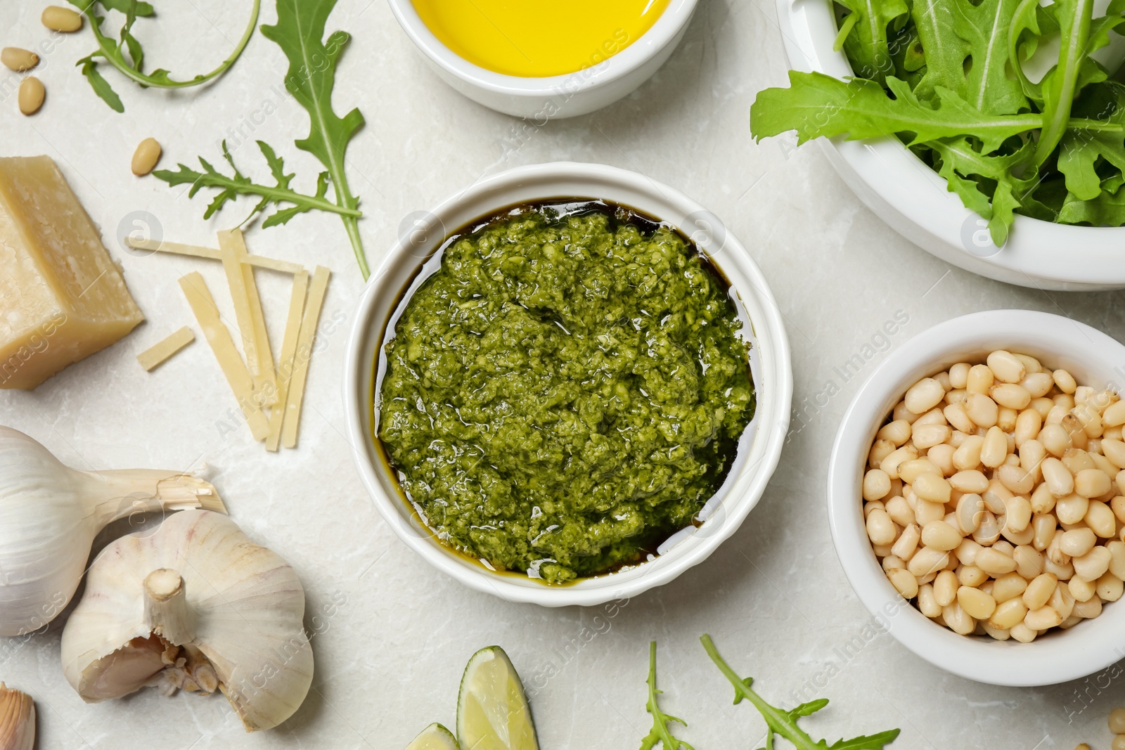 Photo of Bowl of tasty arugula pesto and ingredients on light table, flat lay