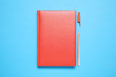 Stylish red notebook and pen on light blue background, flat lay