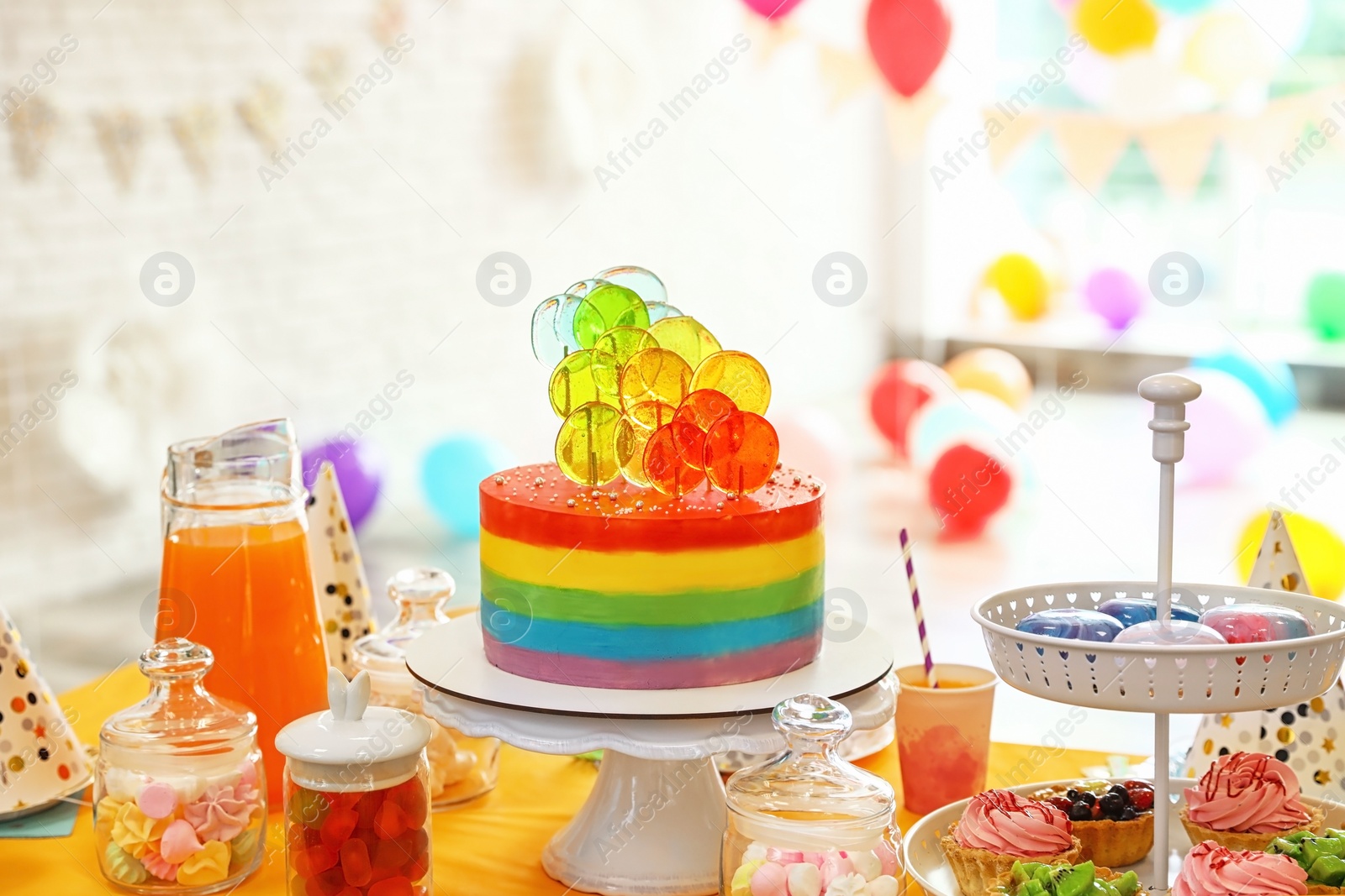 Photo of Bright birthday cake and other treats on table in decorated room