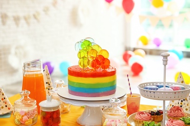 Bright birthday cake and other treats on table in decorated room