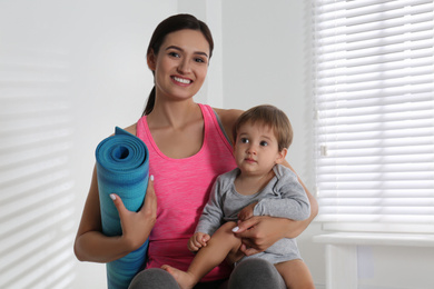 Photo of Young woman in fitness clothes with her son and mat indoors. Home fitness