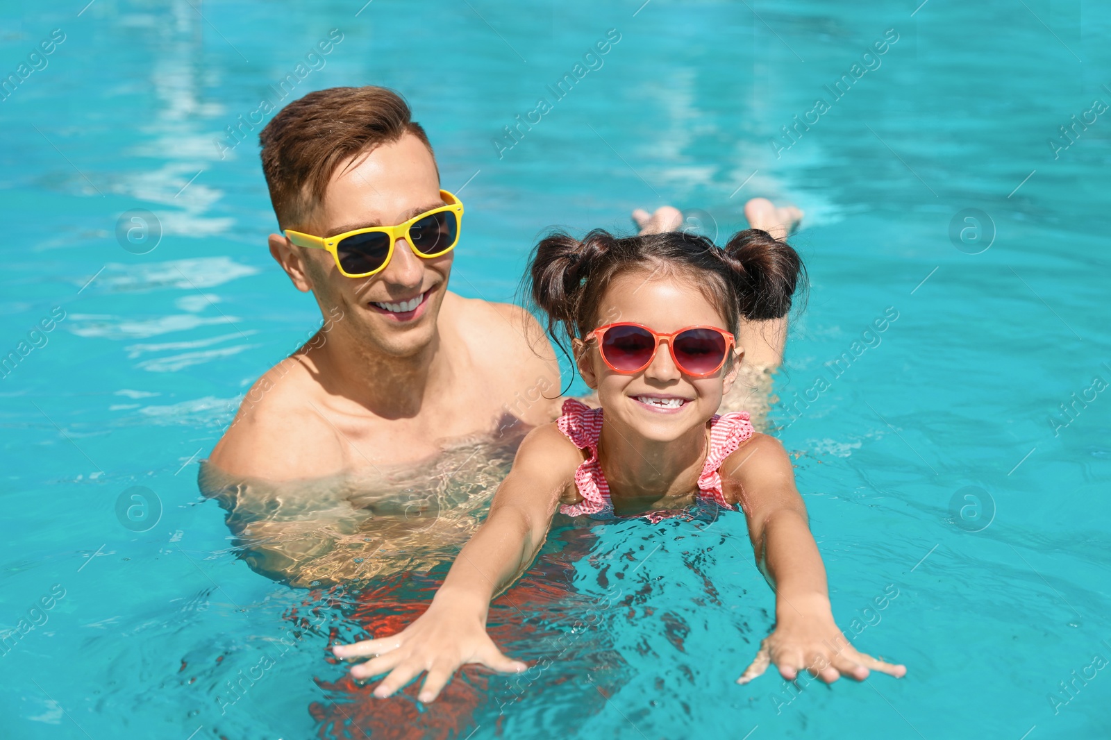 Photo of Young man teaching his daughter to swim in pool
