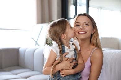Photo of Cute little girl kissing her mother on sofa in living room