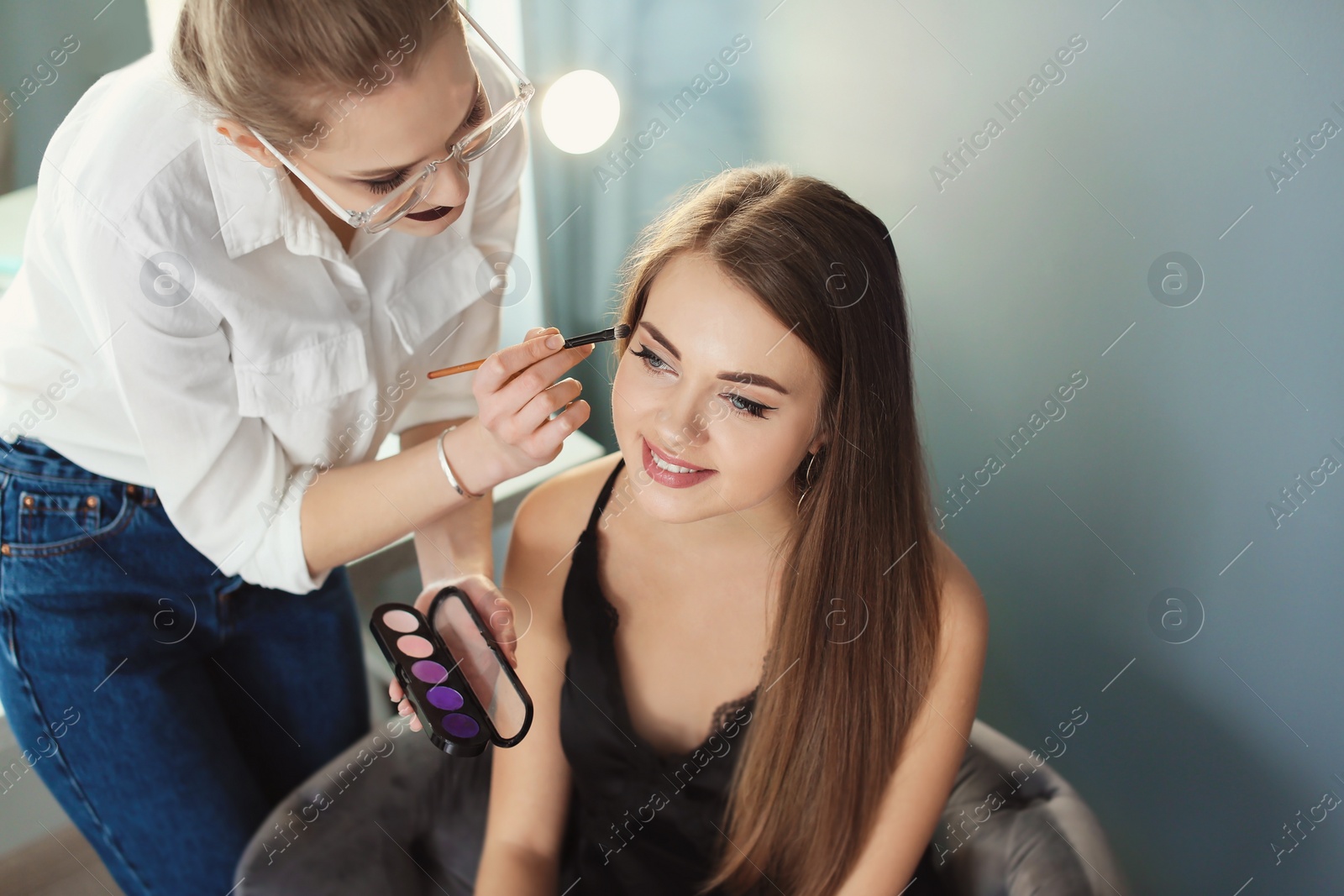 Photo of Professional makeup artist working with beautiful young woman in studio