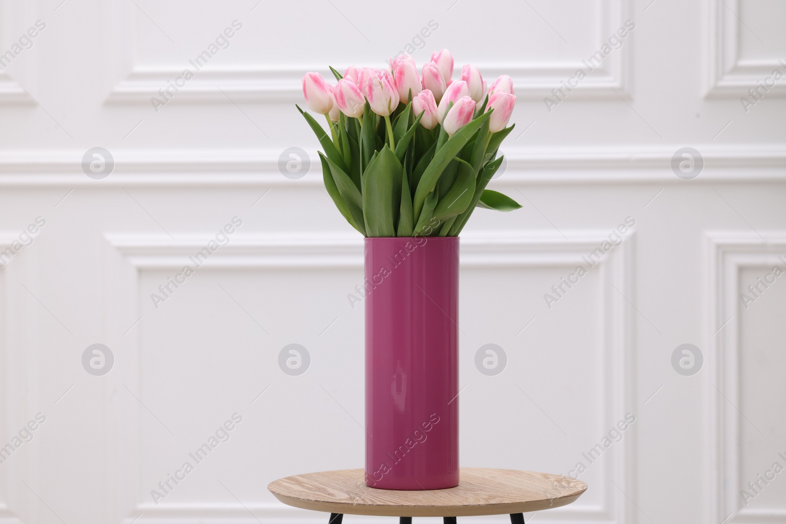 Photo of Beautiful bouquet of fresh pink tulips on table near white wall