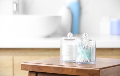 Photo of Plastic jars with cotton pads and swabs on wooden stool in bathroom. Space for text