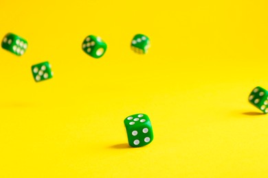 Photo of Many green game dices falling on yellow background