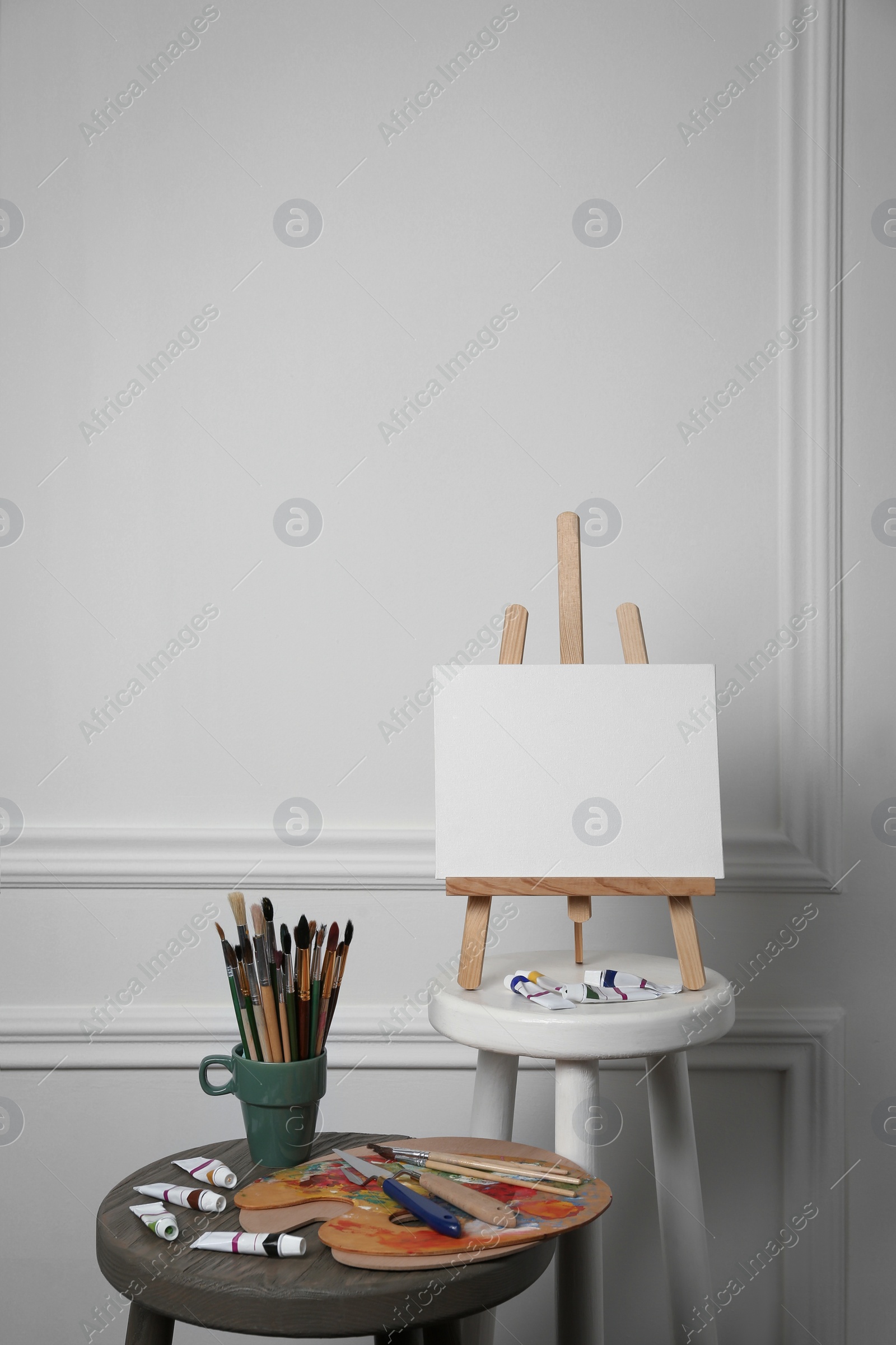 Photo of Easel with blank canvas, brushes, paints and palette in studio