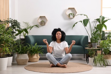 Photo of Relaxing atmosphere. Woman meditating near potted houseplants in room