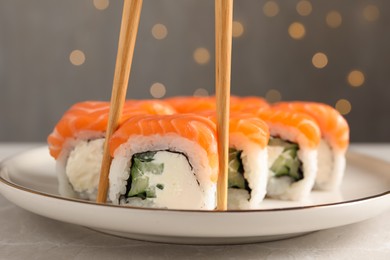 Photo of Tasty sushi rolls and chopsticks on grey table against blurred lights, closeup