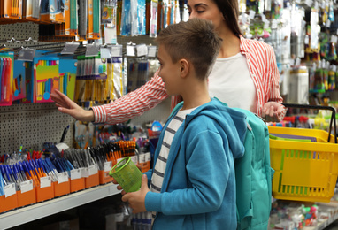 Photo of Little boy with mother choosing school stationery in supermarket
