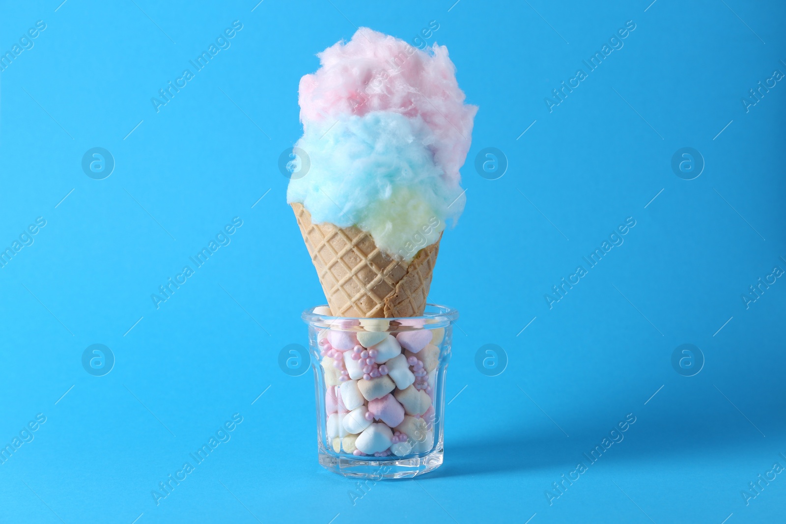 Photo of Sweet cotton candy in waffle cone on light blue background