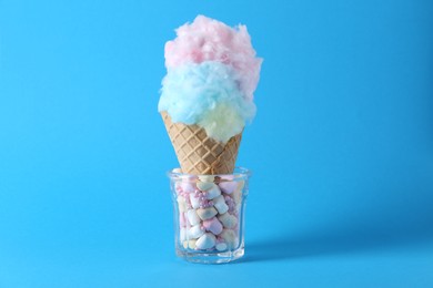 Sweet cotton candy in waffle cone on light blue background