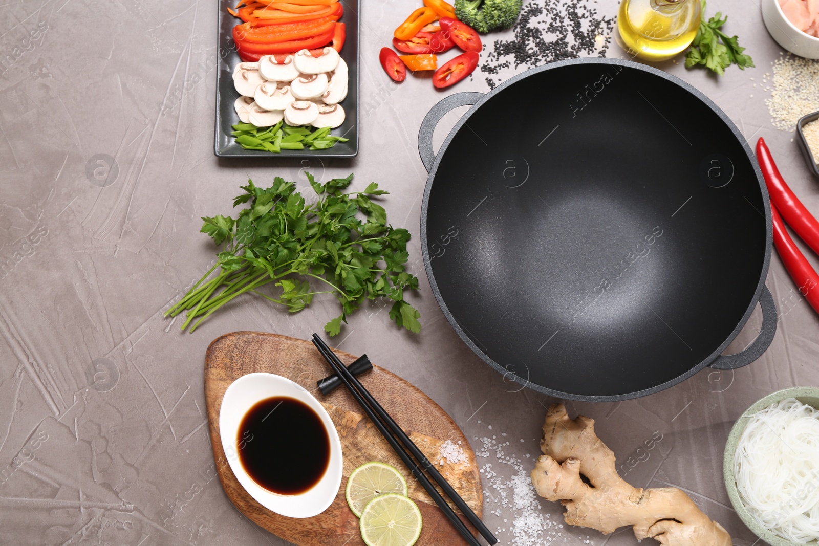 Photo of Wok, chopsticks and different products on grey textured table, flat lay. Space for text