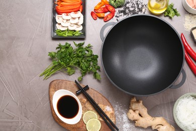 Photo of Wok, chopsticks and different products on grey textured table, flat lay. Space for text