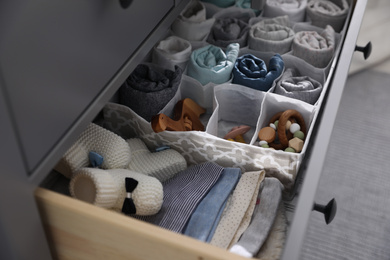 Photo of Modern open chest of drawers with baby clothes and accessories in room, closeup
