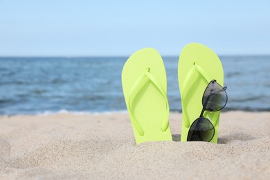 Stylish light green flip flops and sunglasses on beach sand, space for text