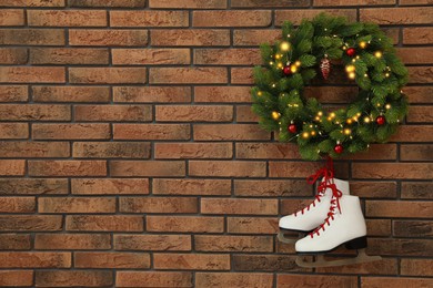 Pair of ice skates and beautiful Christmas wreath hanging on brick wall, space for text