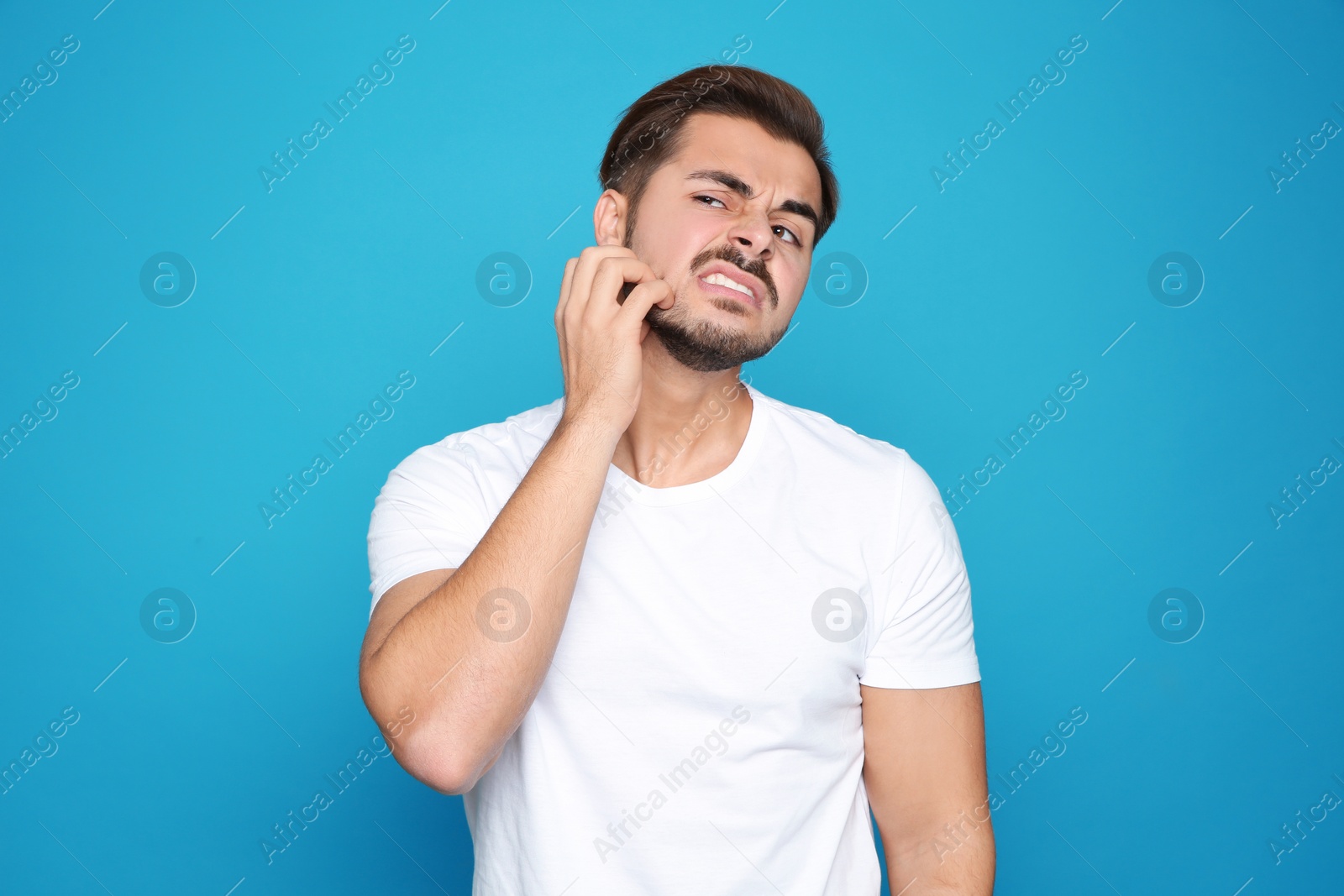 Photo of Young man scratching face on color background. Annoying itch