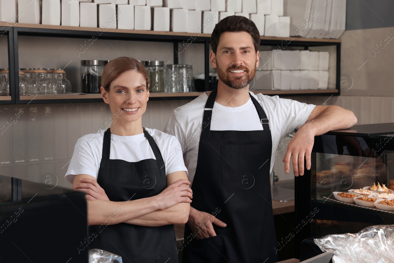 Photo of Happy sellers at cashier desk near showcase in bakery shop