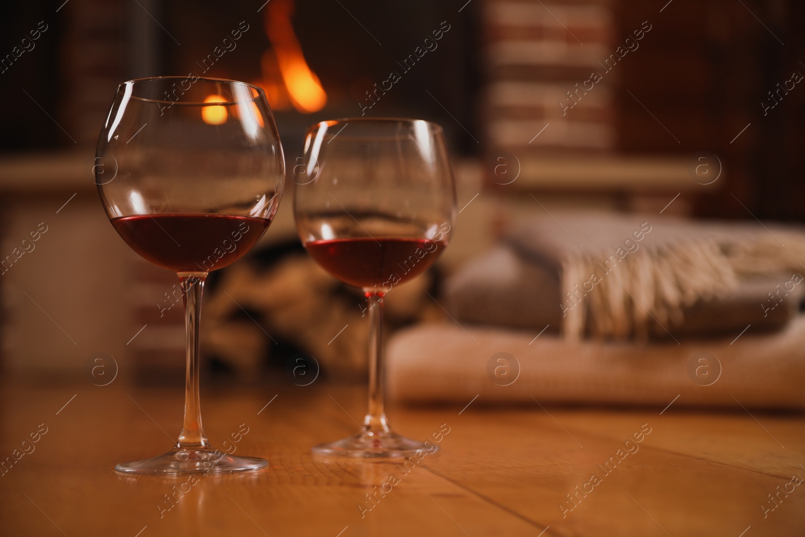 Photo of Glasses of red wine on wooden floor near fireplace. Space for text