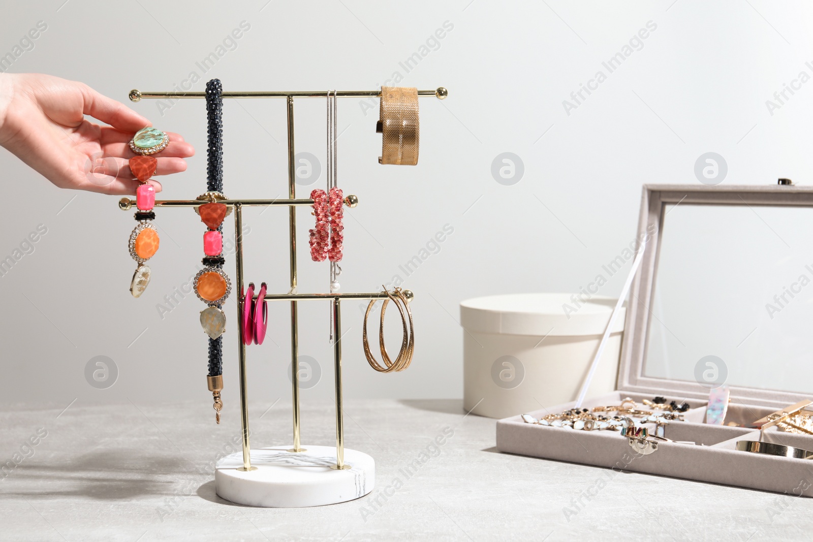 Photo of Woman taking earring from holder with jewelry on light grey table, closeup