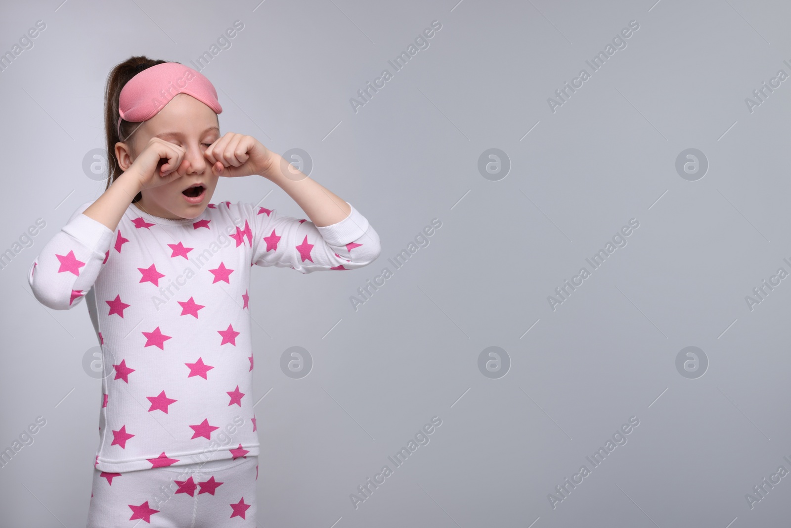 Photo of Girl with sleep mask yawning on light grey background, space for text. Insomnia problem