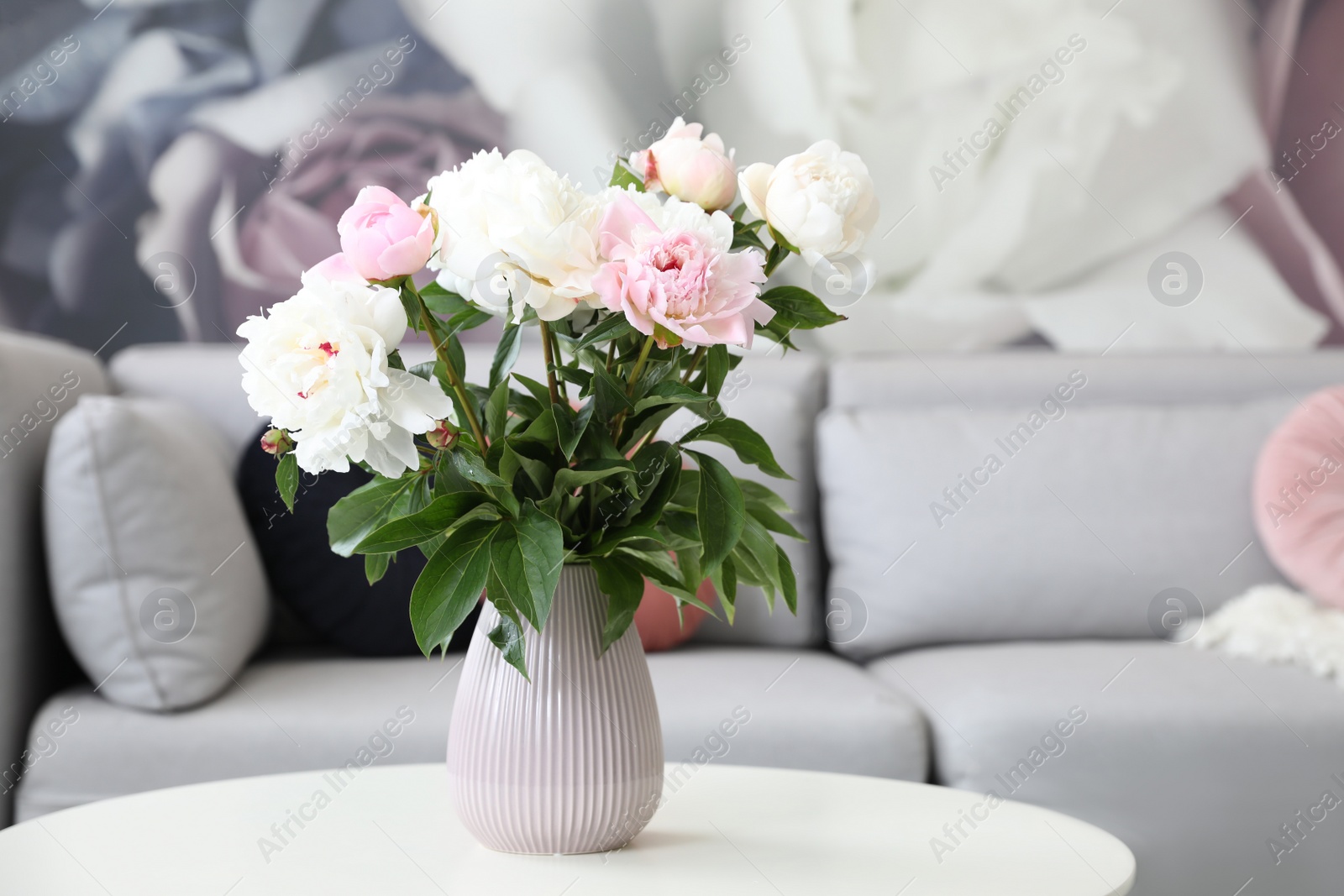 Photo of Bouquet of peonies on table near sofa in modern room. Interior design