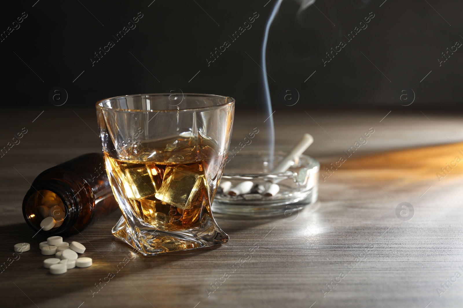 Photo of Alcohol addiction. Whiskey in glass, pills and cigarettes on wooden table, space for text