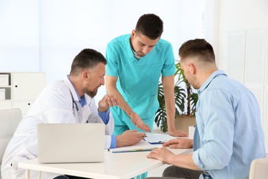 Photo of Male doctor and his assistant working with patient in clinic. Cardiology consultation