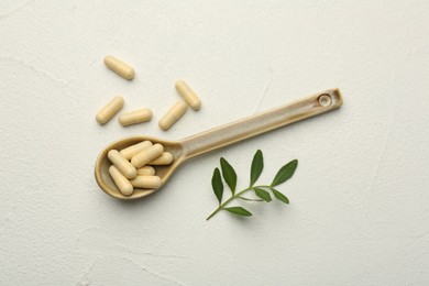 Vitamin capsules in spoon and leaves on white wooden table, flat lay