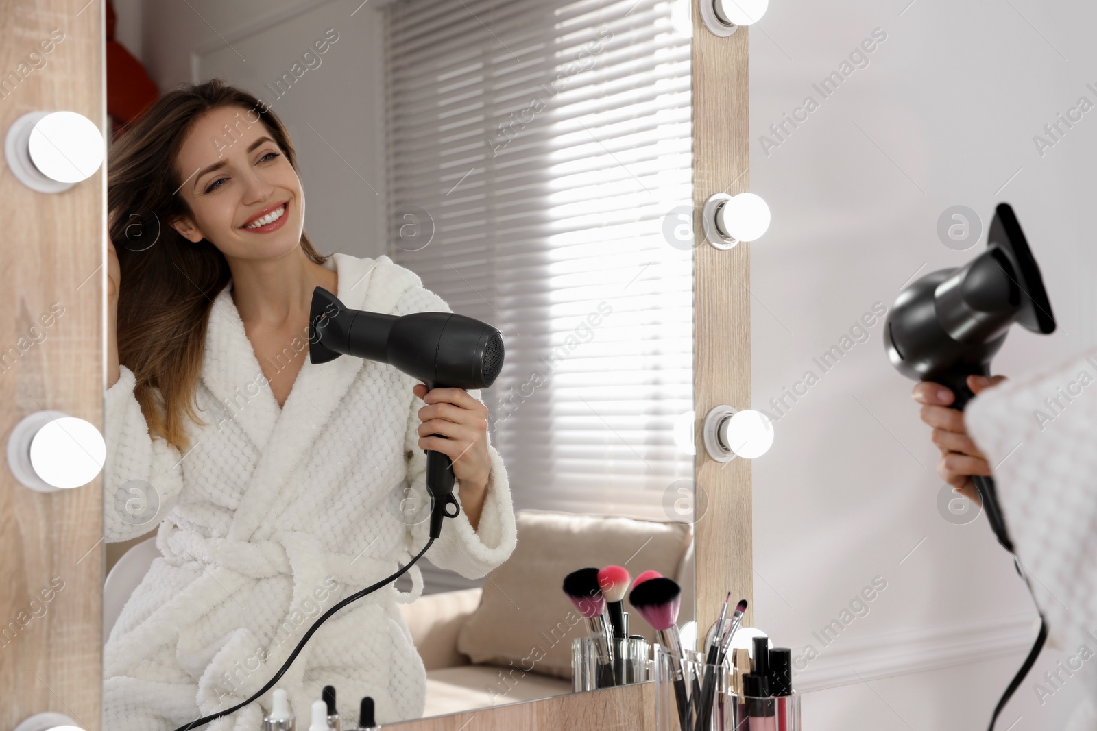 Photo of Beautiful young woman using hair dryer near mirror at home