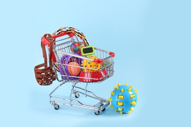 Photo of Different pet goods in shopping cart on light blue background. Shop items