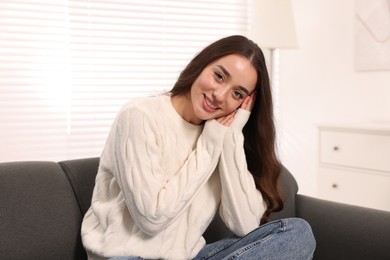 Photo of Beautiful young woman in stylish warm sweater on sofa at home