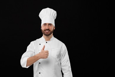 Photo of Smiling mature male chef showing thumbs up on black background, space for text