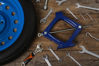 Car wheel, scissor jack and different tools on wooden surface, flat lay