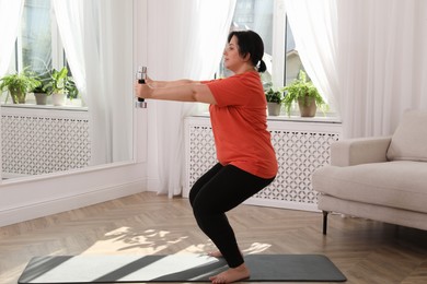 Overweight mature woman doing exercise with dumbbells at home