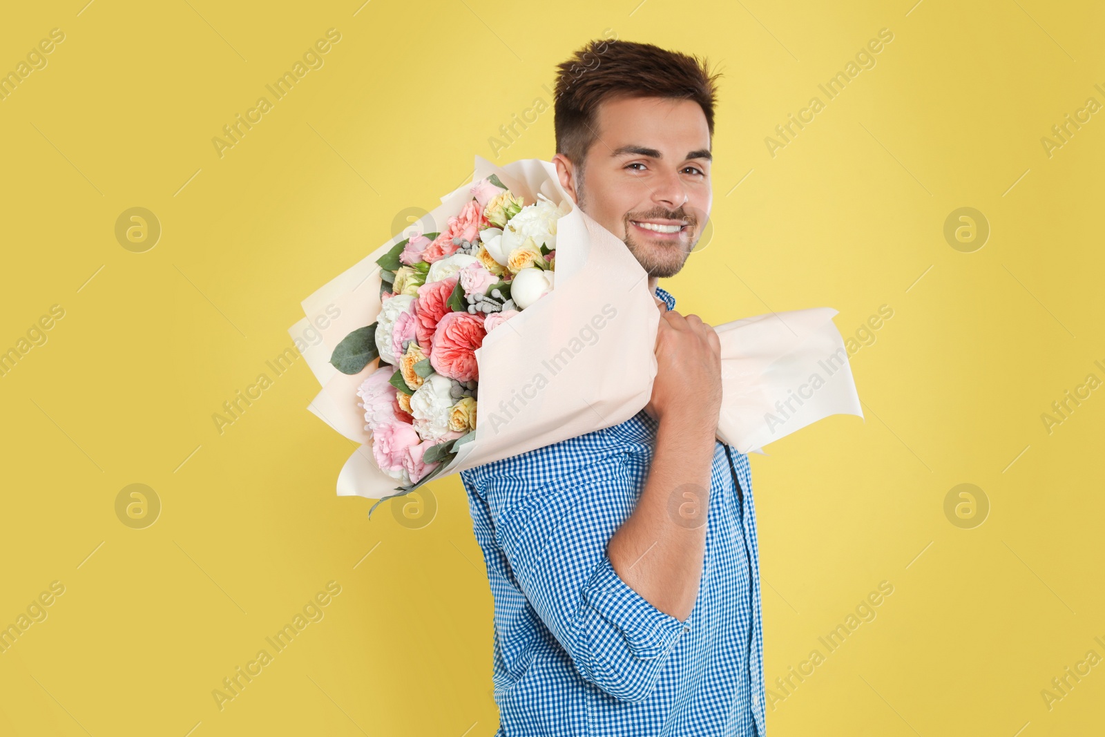 Photo of Young handsome man with beautiful flower bouquet on yellow background