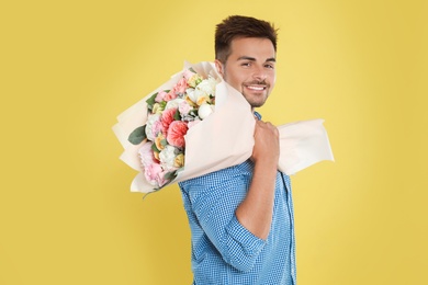 Young handsome man with beautiful flower bouquet on yellow background