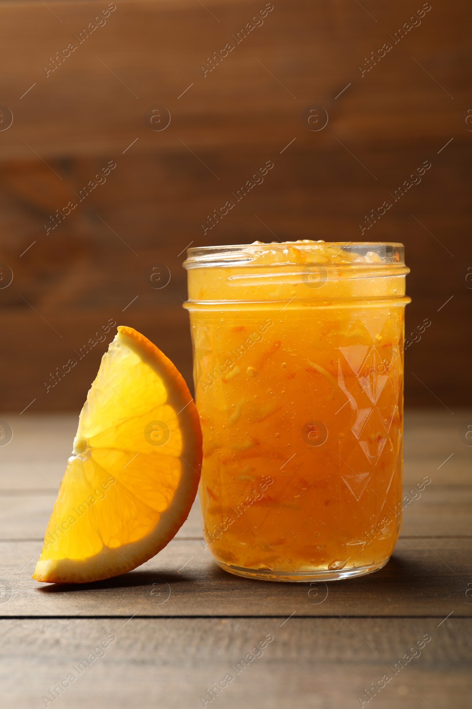 Photo of Delicious orange marmalade and citrus fruit slice on wooden table
