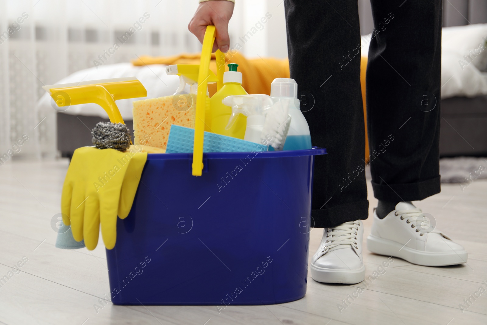 Photo of Woman with different cleaning supplies in bucket on floor at home, closeup