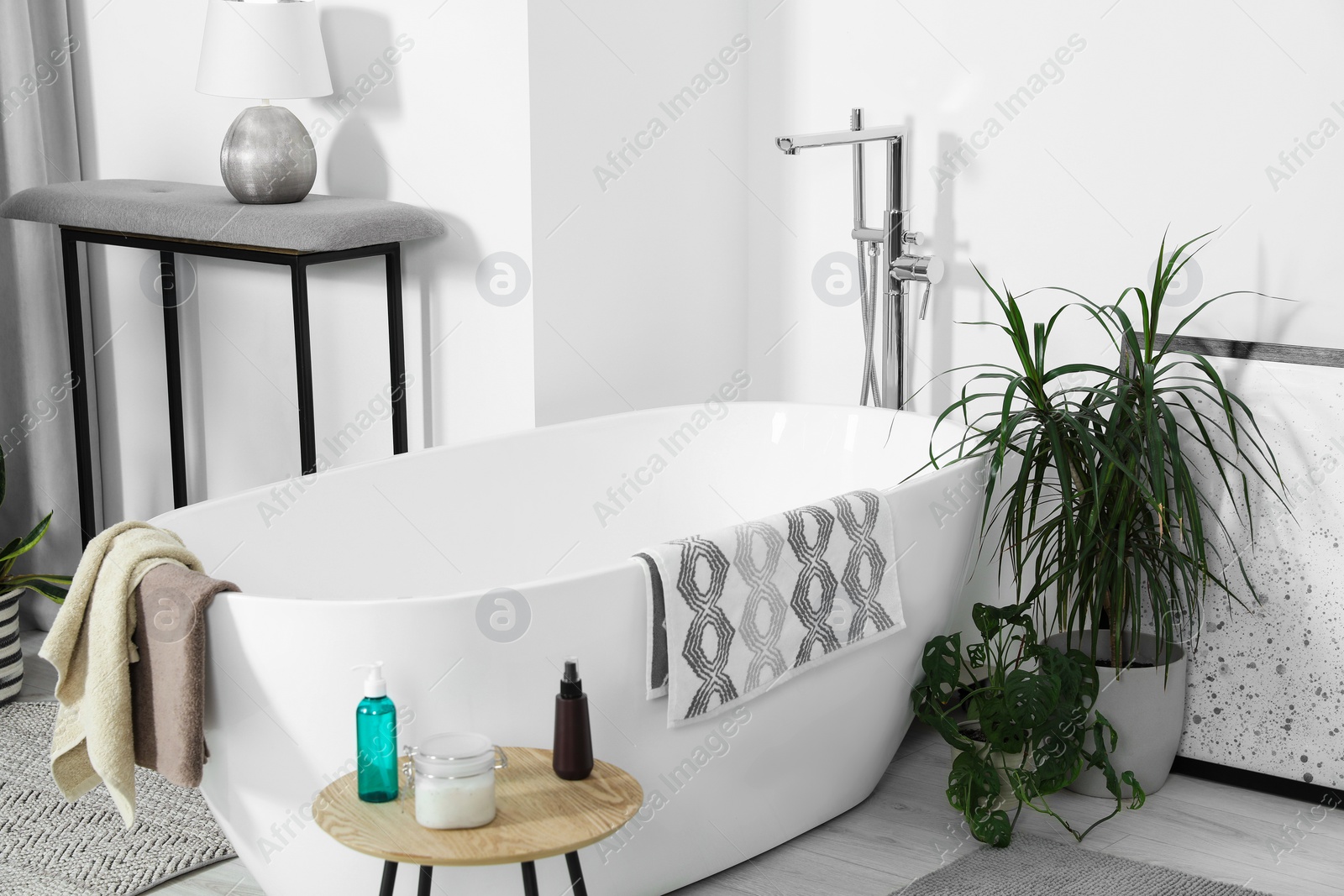 Photo of Stylish white tub and wooden table with toiletries in bathroom. Interior design