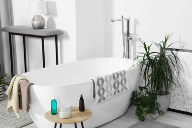 Stylish white tub and wooden table with toiletries in bathroom. Interior design