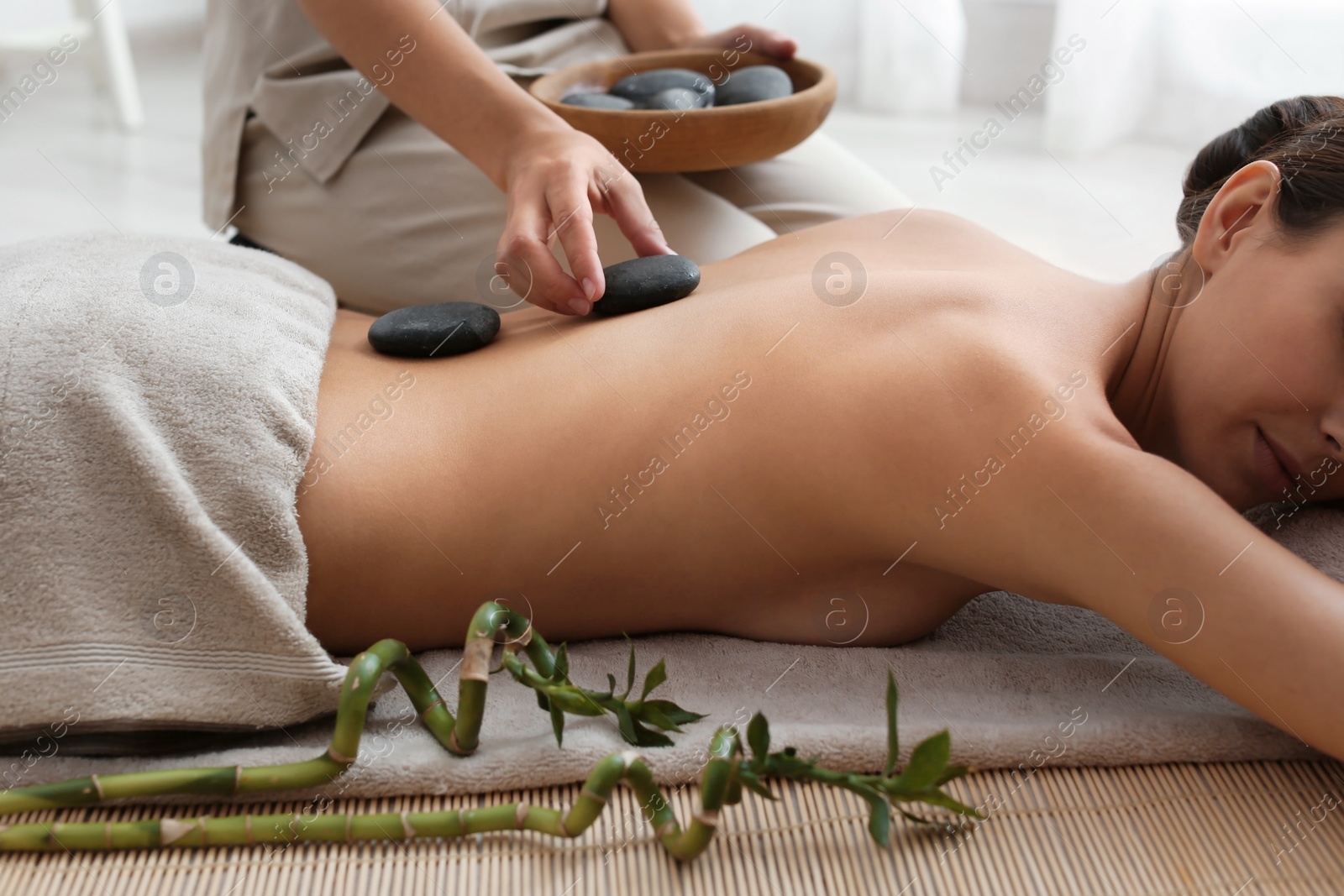 Photo of Beautiful young woman getting hot stone massage in spa salon