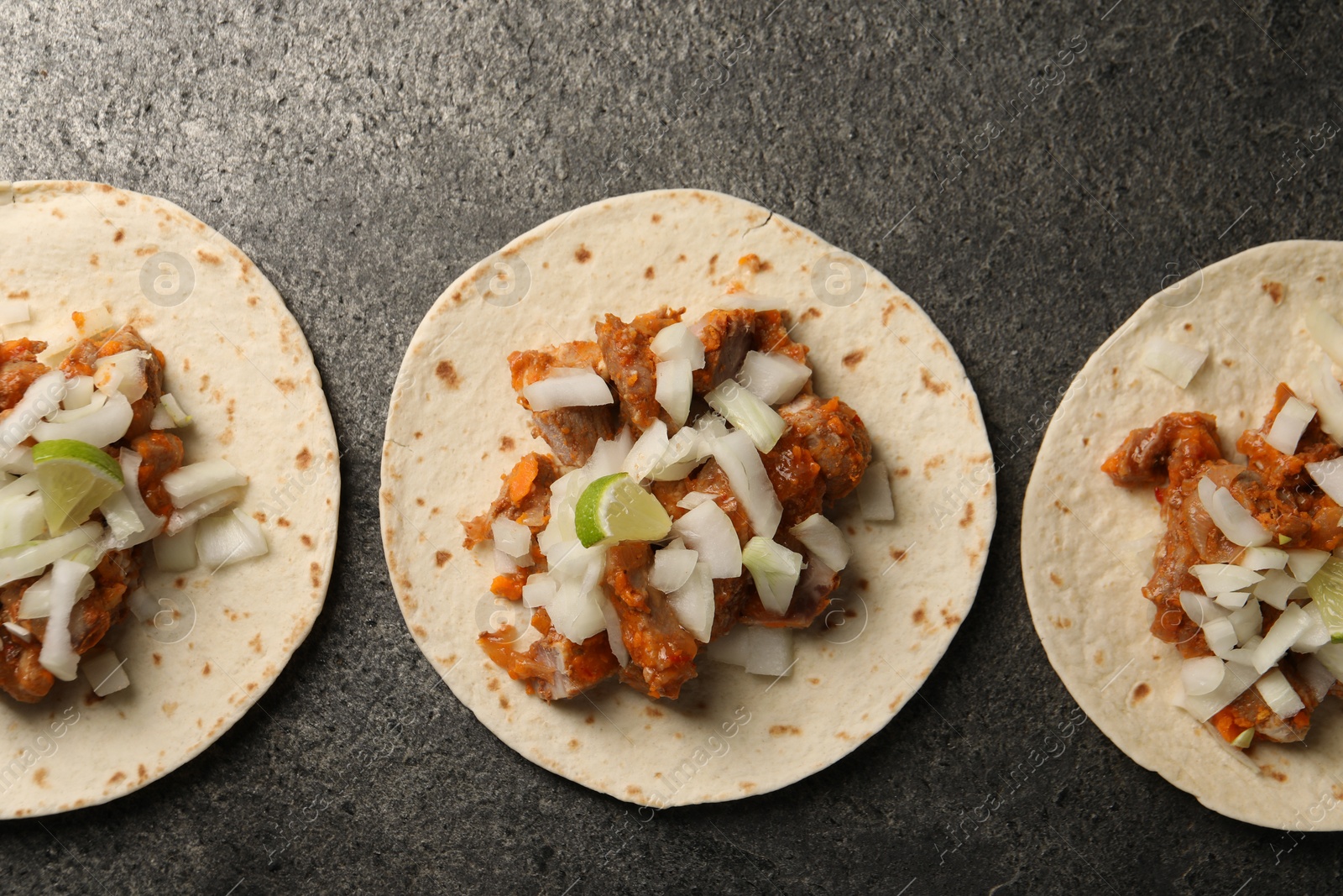 Photo of Delicious tacos with vegetables, meat and lime on grey textured table, flat lay