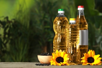 Photo of Bottles of cooking oil, sunflowers and seeds on wooden table against blurred background, space for text