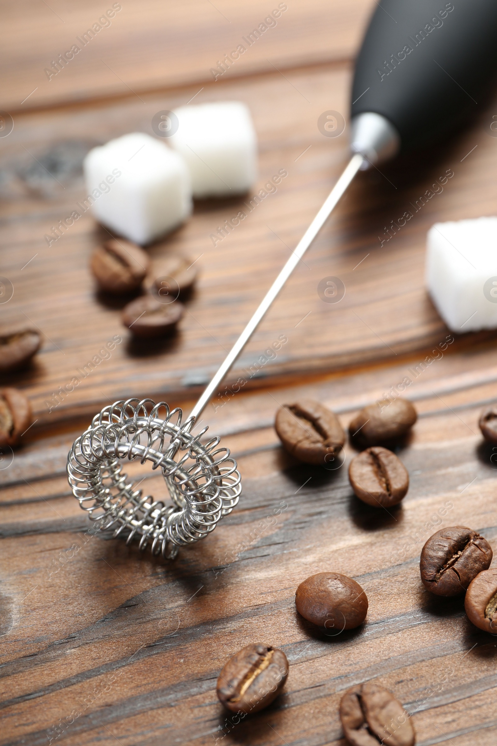 Photo of Black milk frother wand, sugar cubes and coffee beans on wooden table, closeup