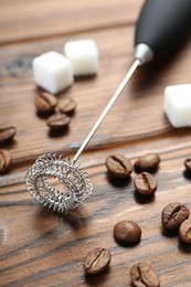 Black milk frother wand, sugar cubes and coffee beans on wooden table, closeup