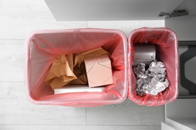 Open cabinet with full trash bins for separate waste collection in kitchen, top view