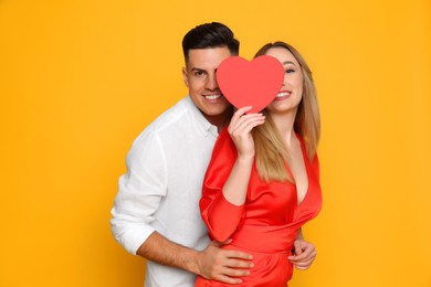 Photo of Lovely couple with decorative heart on yellow background. Valentine's day celebration